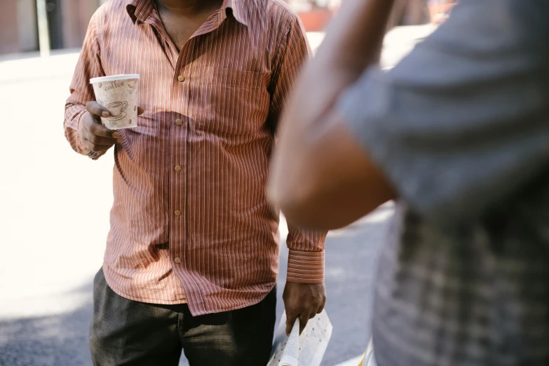 a man talking on a cell phone while holding a cup of coffee, pexels contest winner, on an indian street, red shirt brown pants, malnourished, two young men