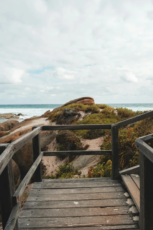 a wooden walkway leading to a beach next to the ocean, by Lucas Vorsterman, unsplash, boulders, staircase, lachlan bailey, rock roof