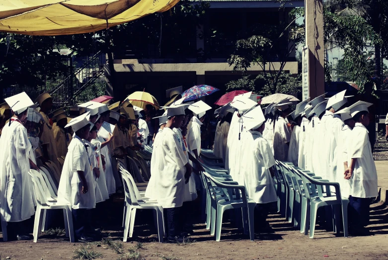 a group of people wearing graduation gowns and holding umbrellas, a colorized photo, unsplash, philippines, praying, white coat, ((oversaturated))