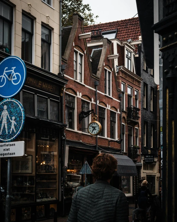 a woman walking down a street next to tall buildings, by Jan Tengnagel, view of houses in amsterdam, thumbnail, traffic signs, stores