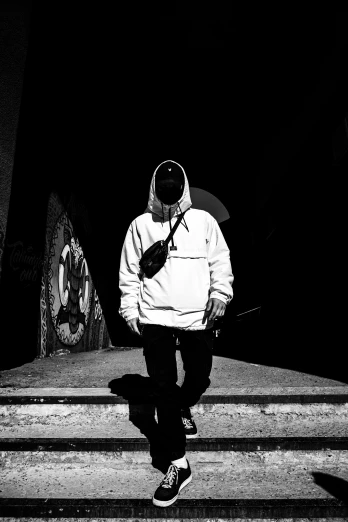 a black and white photo of a man walking down a set of stairs, a black and white photo, unsplash, graffiti, wearing a hood with pointy ears, high-contrast lighting, an all white human, wearing a hoody
