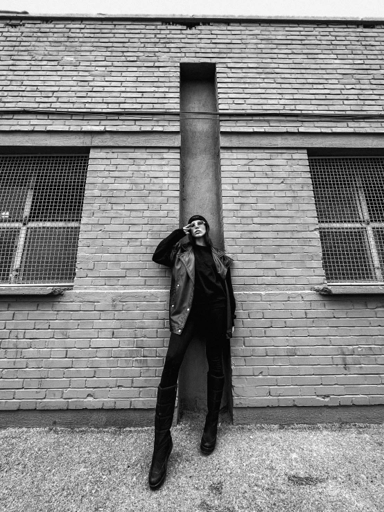 a black and white photo of a woman leaning against a building, unsplash, conceptual art, dressed in black leather, androgynous male, anna nikonova aka newmilky, musician