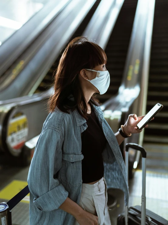 a woman wearing a face mask standing next to an escalator, a picture, trending on pexels, happening, square, she is holding a smartphone, scientific photo, dark. no text