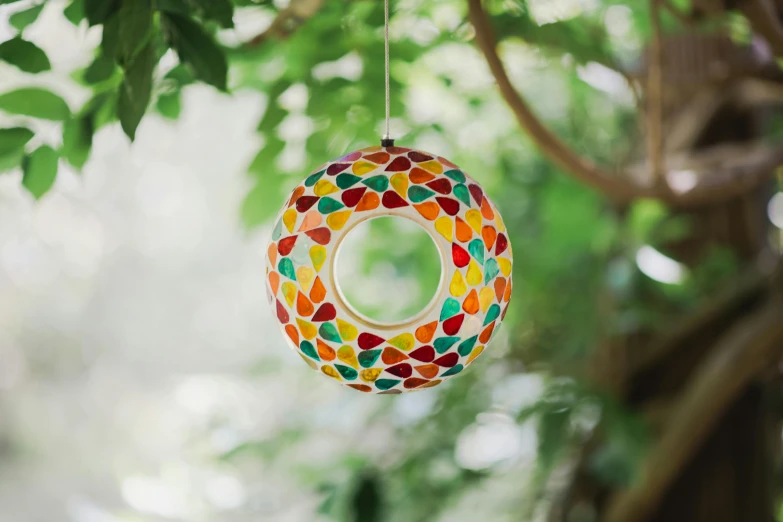 a colorful stained glass circle hanging from a tree, inspired by Damien Hirst, arabesque, outdoor lighting, multi - coloured, donut, multi colour