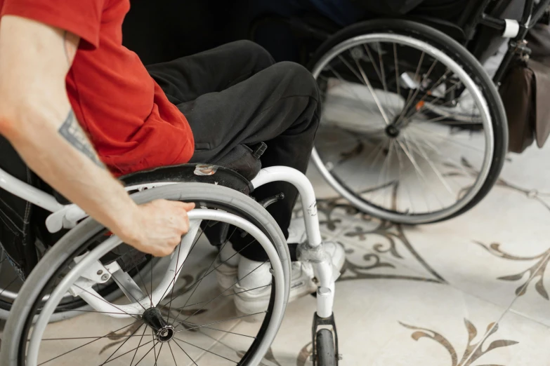 a man in a red shirt sitting in a wheel chair, by Julia Pishtar, trending on pexels, hurufiyya, two arms and to legs, sitting on the floor, levers, coloured