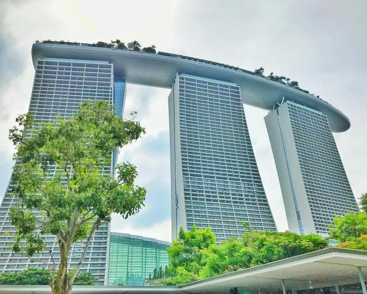 a very tall building with a lot of trees in front of it, inspired by Tadao Ando, pexels contest winner, singapore esplanade, white sweeping arches, 🐝👗👾, two organic looking towers