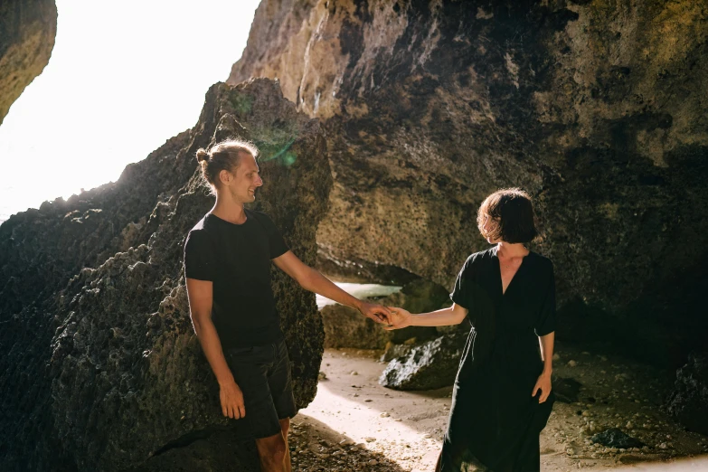 a man and a woman holding hands on a beach, a portrait, by Lee Loughridge, pexels contest winner, natural cave wall, thumbnail, black, smiling at each other