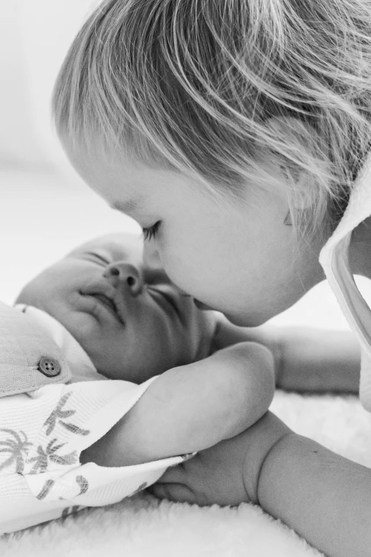 a black and white photo of a little girl kissing a baby, symbolism, profile image, little brother, nursing, lachlan bailey