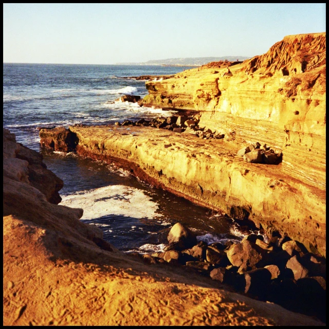 a large body of water next to a rocky shore, an album cover, golden hour in pismo california, between sedimentary deposits, lomography, staggered terraces