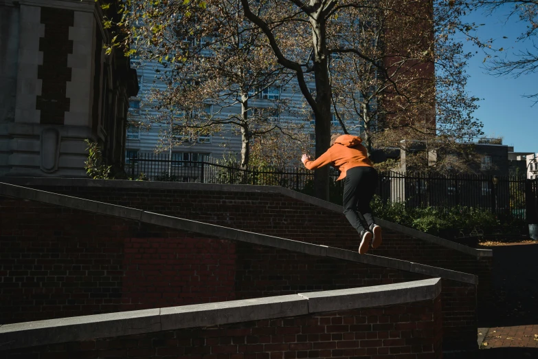 a man flying through the air while riding a skateboard, by Daniel Seghers, unsplash contest winner, long orange sweatshirt, in new york city, penrose stairs, 5k