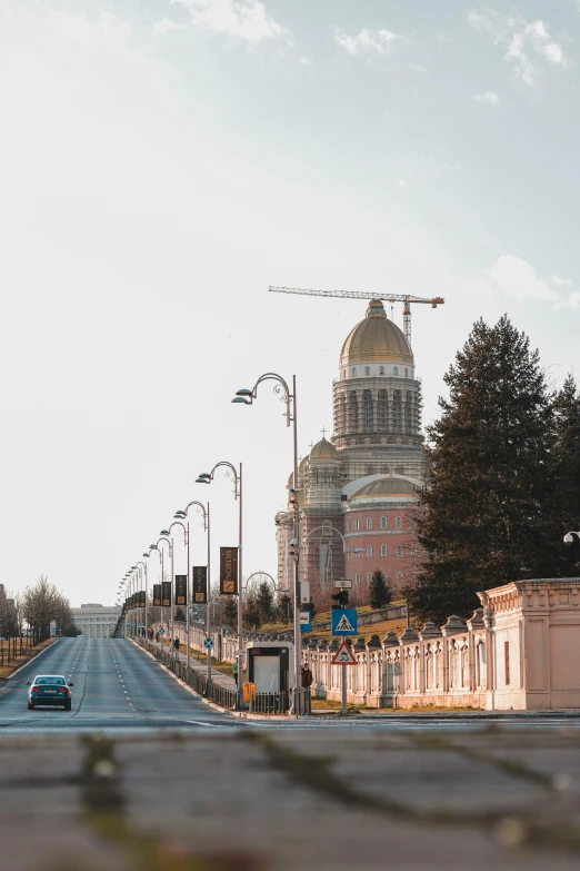 a car driving down a street next to a tall building, unsplash contest winner, socialist realism, neoclassical tower with dome, idaho, low quality photo, golden pillars