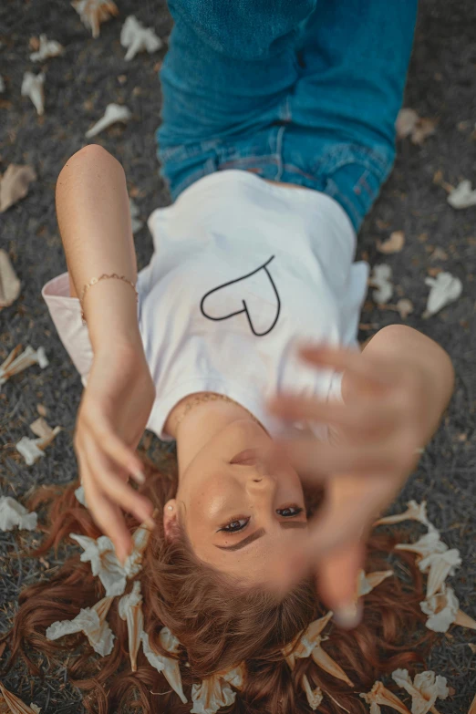 a woman laying on the ground with her hands in the air, trending on pexels, heart shaped face, jeans and t shirt, white clothing, pixvy