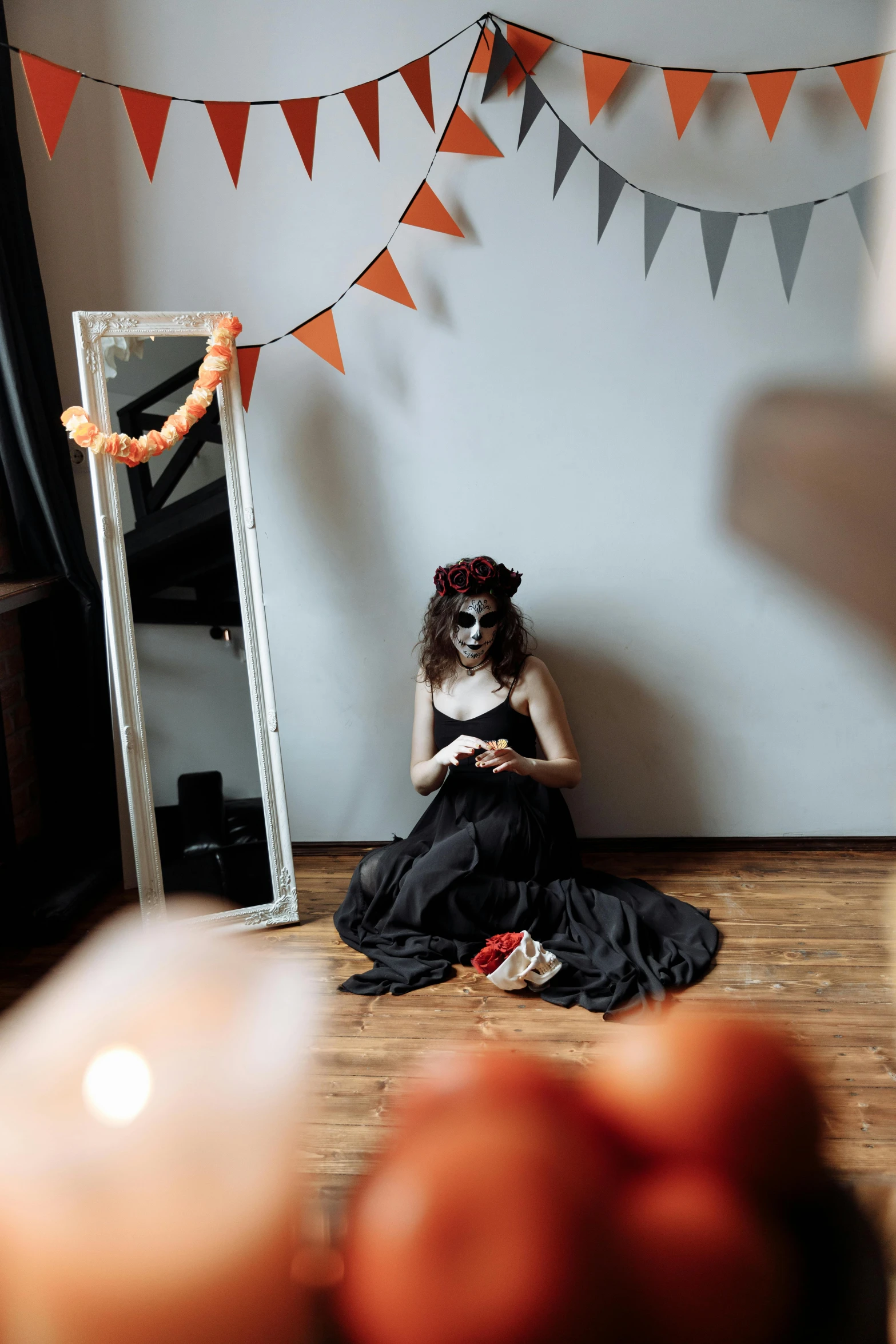 a woman sitting on the floor in front of a mirror, by Lucia Peka, pexels contest winner, gothic art, celebrating day of the dead, dark grey and orange colours, decoration around the room, fancy dress