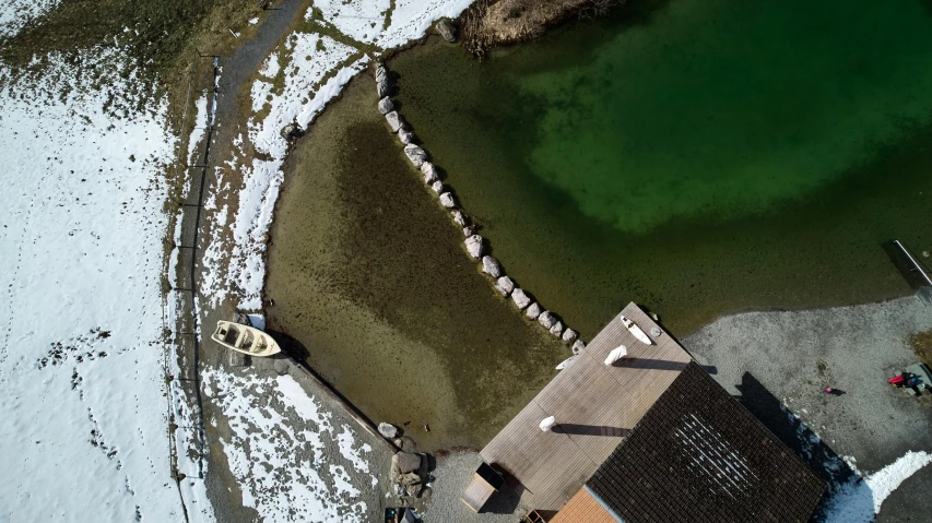 an aerial view of a house next to a body of water, by Jens Søndergaard, pexels contest winner, land art, spring winter nature melted snow, with water and boats, full of greenish liquid, small dock