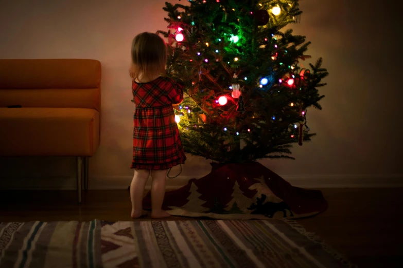 a little girl standing in front of a christmas tree, by Julia Pishtar, pexels contest winner, square, multicoloured, black fir, decoration around the room