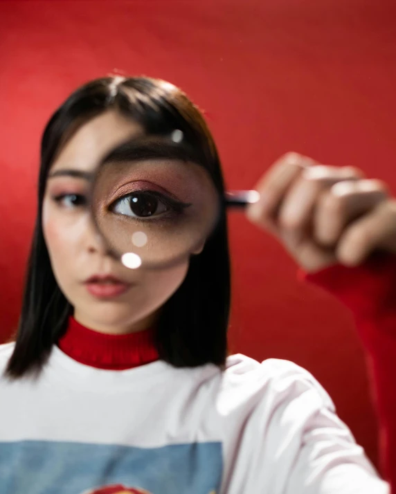 a woman looking through a magnifying glass, trending on pexels, hyperrealism, on a red background, with big eyes, asian features, lgbtq