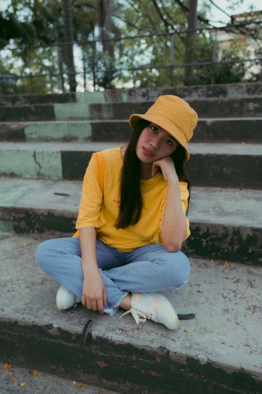 a woman sitting on some steps talking on a cell phone, pexels contest winner, yellow cap, wearing a modern yellow tshirt, pokimane, stoic pose