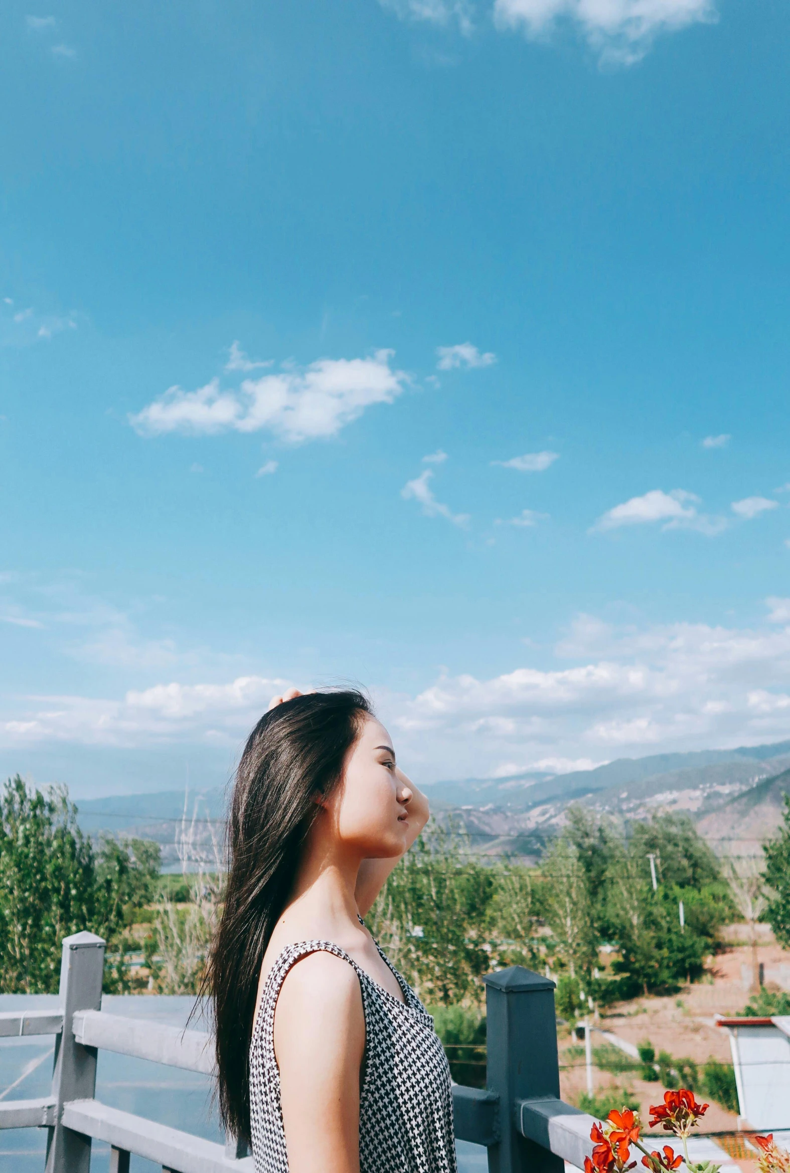 a woman standing on top of a wooden deck, inspired by Ma Yuanyu, trending on unsplash, cloudless blue sky, long flat hair, with mountains as background, background image