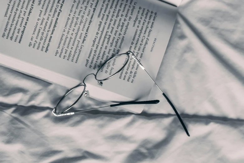 a book sitting on top of a bed next to a pair of glasses, a black and white photo, pexels contest winner, photorealism, silver，ivory, thin round glasses, instagram post, student