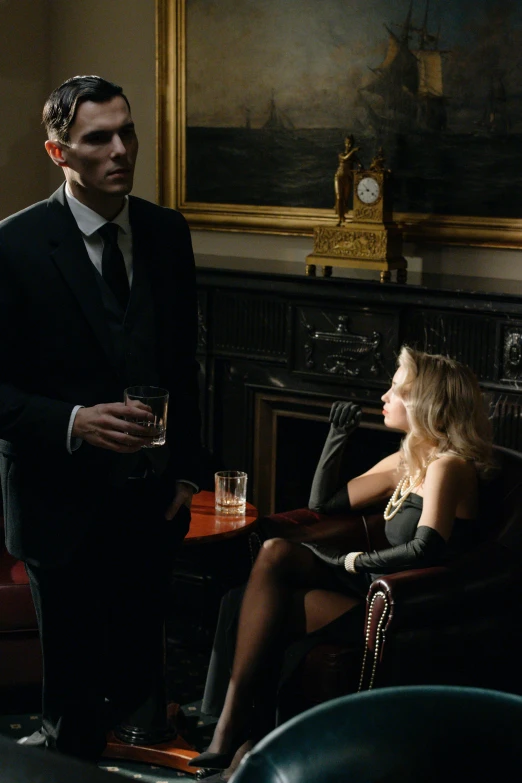 a woman sitting in a chair next to a man in a suit, by David Donaldson, trending on cg society, renaissance, peaky blinders, with a drink, a blond, 7 0 mm. dramatic lighting