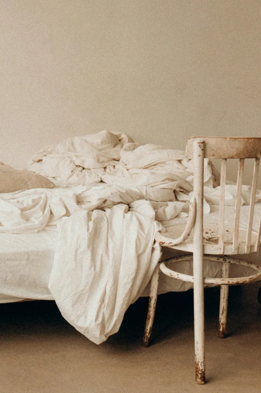 a bed sitting in a bedroom next to a chair, by Elsa Bleda, trending on unsplash, arte povera, ripped up white garment, 1850s, two exhausted, isolated