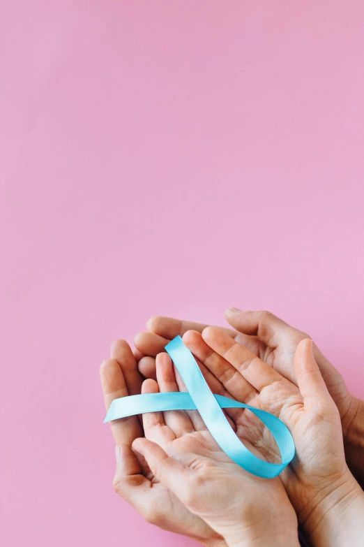 two hands holding a blue ribbon against a pink background, pexels contest winner, happening, light blue skin, maternal, tumours, black and teal paper