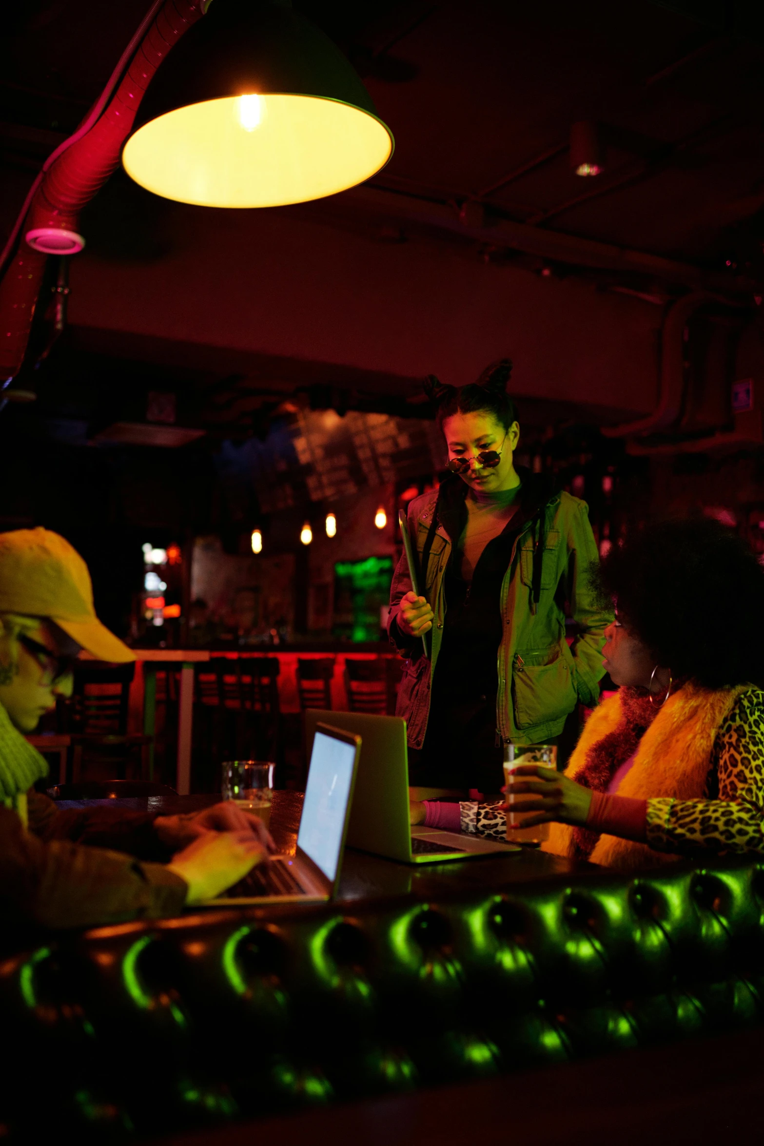 a group of people sitting around a table with a laptop, dramatic neon lighting, background bar, afro tech, frightening surroundings