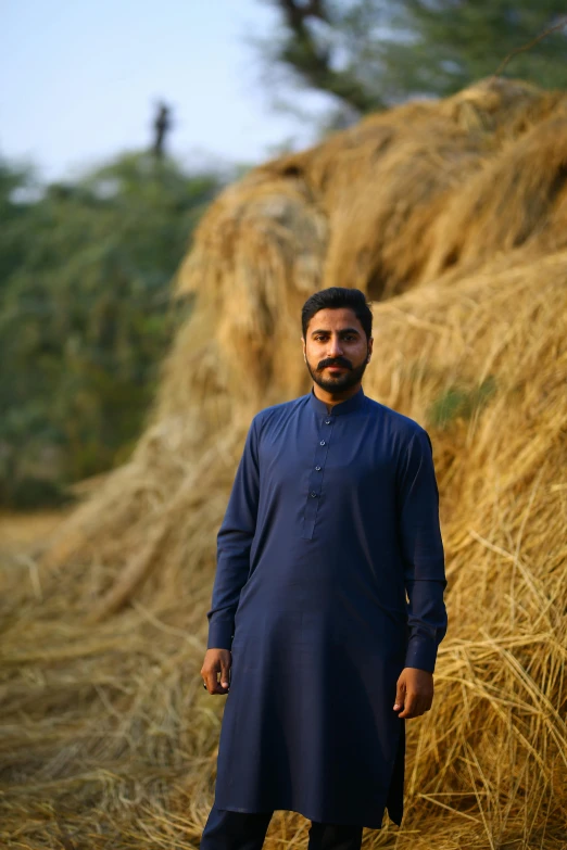 a man standing in front of a pile of hay, by Riza Abbasi, wearing a kurta, navy, profile image, show