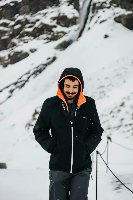 a man riding skis on top of a snow covered slope, wearing jeans and a black hoodie, mutahar laughing, black and orange coat, 2019 trending photo