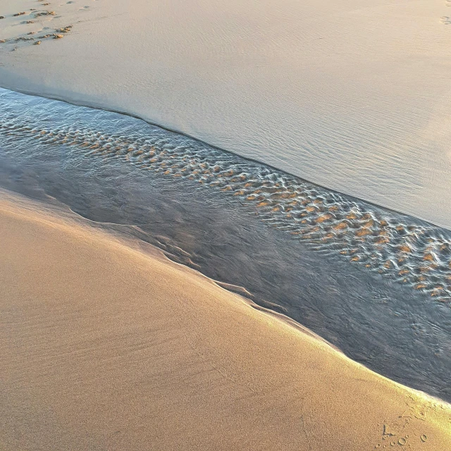 a person riding a surfboard on top of a sandy beach, by Julian Allen, pexels contest winner, land art, erosion channels river, light reflection, sand texture, first light