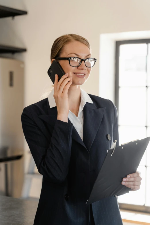 a woman standing in a kitchen talking on a cell phone, in suit with black glasses, selling insurance, developers, holding a clipboard