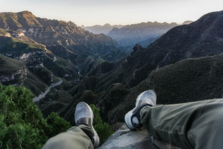 a person sitting on the edge of a cliff overlooking a valley, inspired by Zhang Kechun, pexels contest winner, realism, sneaker photo, lying down, the great wall, detailed shot legs-up