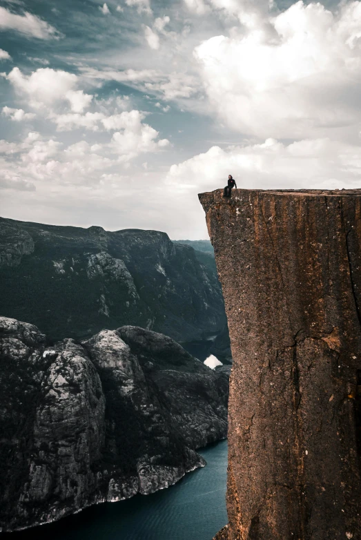 a person standing on the edge of a cliff, by Jesper Knudsen, pexels contest winner, realism, big sharp rock, sitting down, extreme panoramic, high angle vertical