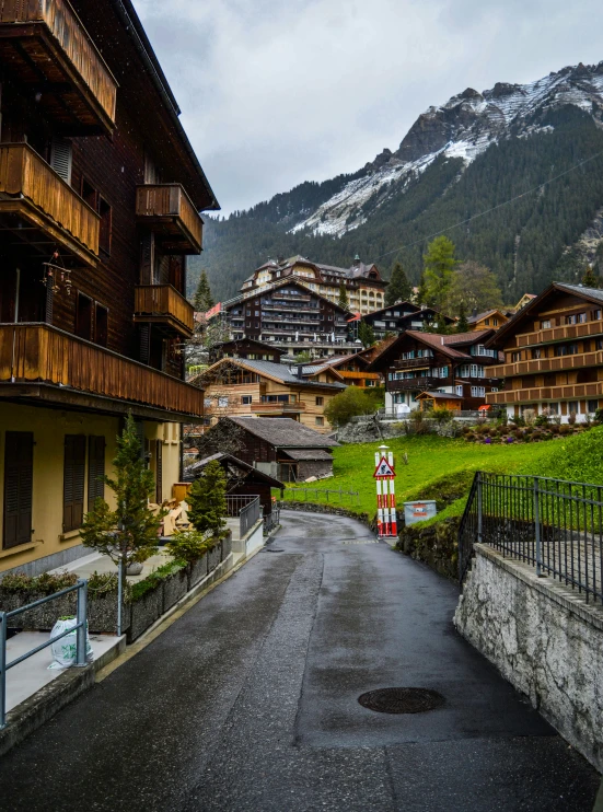 a street lined with wooden buildings next to a lush green hillside, by Daniel Seghers, pexels contest winner, swiss alps, slide show, high rises, 1 2 9 7