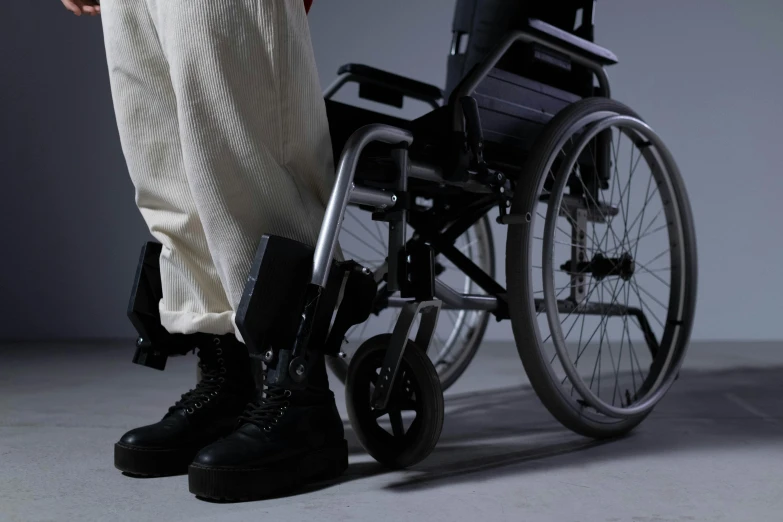 a person standing next to a wheel chair, hurufiyya, heavy-duty boots, [ realistic photography ], lit from the side, up-close