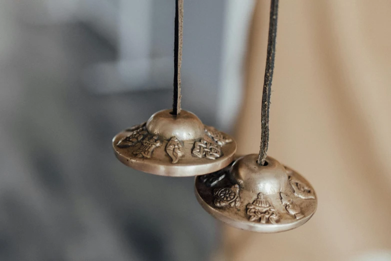 a couple of bells hanging from a string, inspired by Gong Kai, baroque, detailed product shot, bronze, up close shot, silver