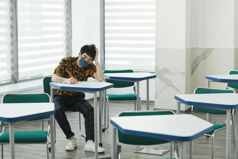 a man sitting at a desk with a mask on his face, by Jang Seung-eop, trending on pexels, paris school, sitting alone, schools, sittin, grading