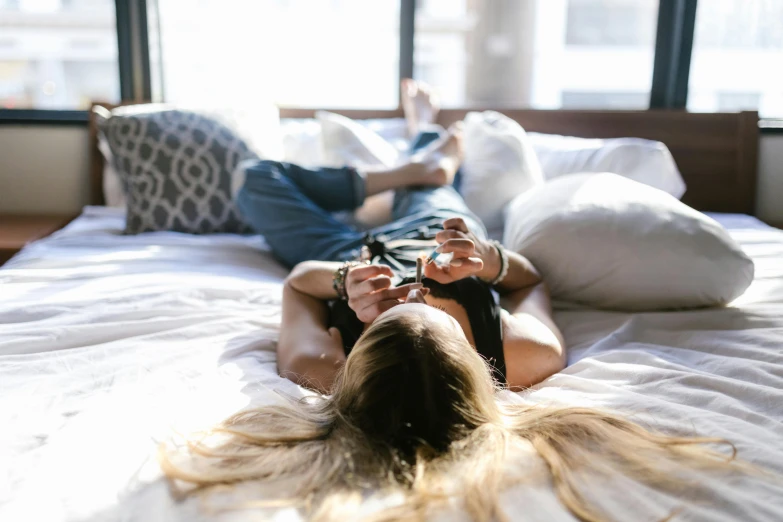 a woman laying on top of a bed next to a window, inspired by Elsa Bleda, trending on pexels, happening, messy blond hair, wearing black choker, teenager hangout spot, overexposed