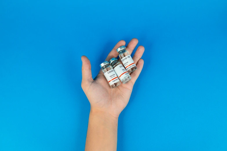 a hand holding a bunch of pills on a blue background, by Julia Pishtar, pexels contest winner, bottles, mini model, 3/4 front view, medical labels