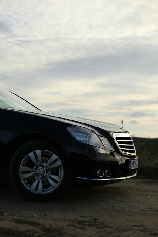 a black car parked on the side of a dirt road, very elegant features, close-up!!!!!, sky line, elegantly dressed