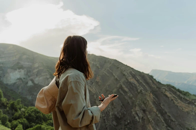 a woman standing on top of a mountain looking at her cell phone, trending on pexels, happening, girl with brown hair, a person standing in front of a, morning, walking to the right