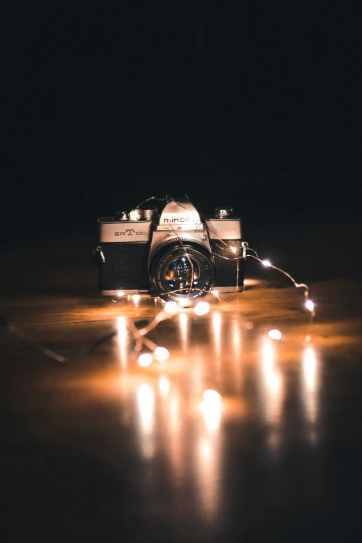 a camera sitting on top of a wooden table, by Niko Henrichon, unsplash contest winner, fairy lights, medium format, string lights, profile picture