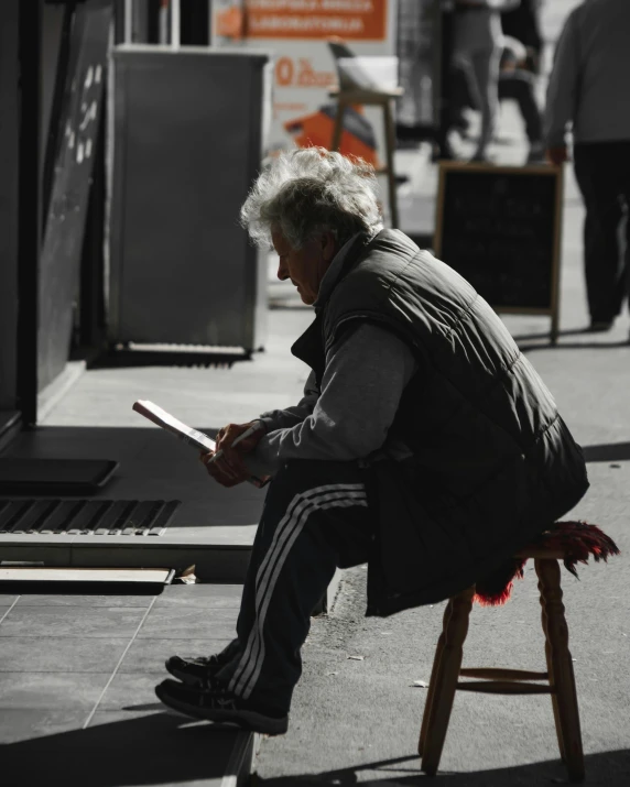 a man sitting on a stool reading a book, pexels contest winner, street art, old gray hair, melbourne, lgbtq, writing a letter