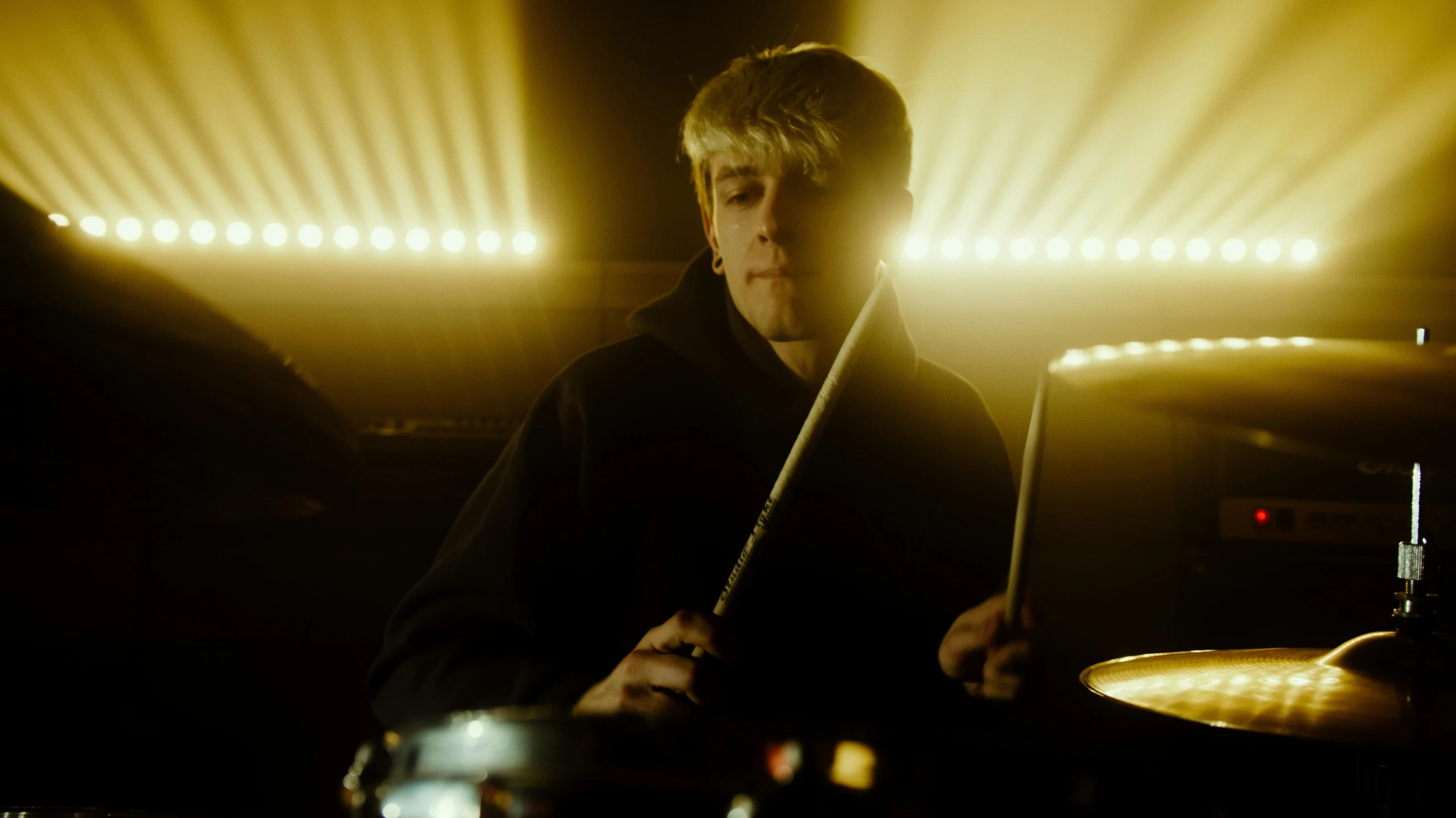 a man playing drums in a dimly lit room, by Dicky Doyle, realism, yung lean, a blond, ( ( theatrical ) ), looking to his side