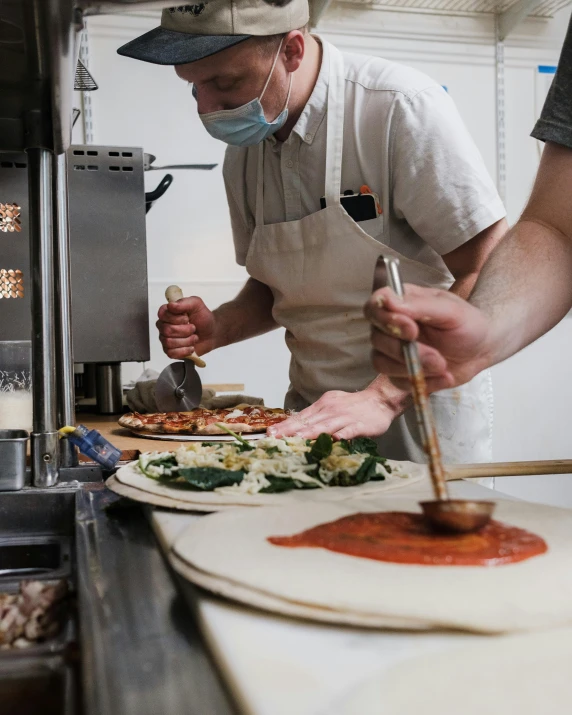 a couple of people preparing food in a kitchen, pizza on a table