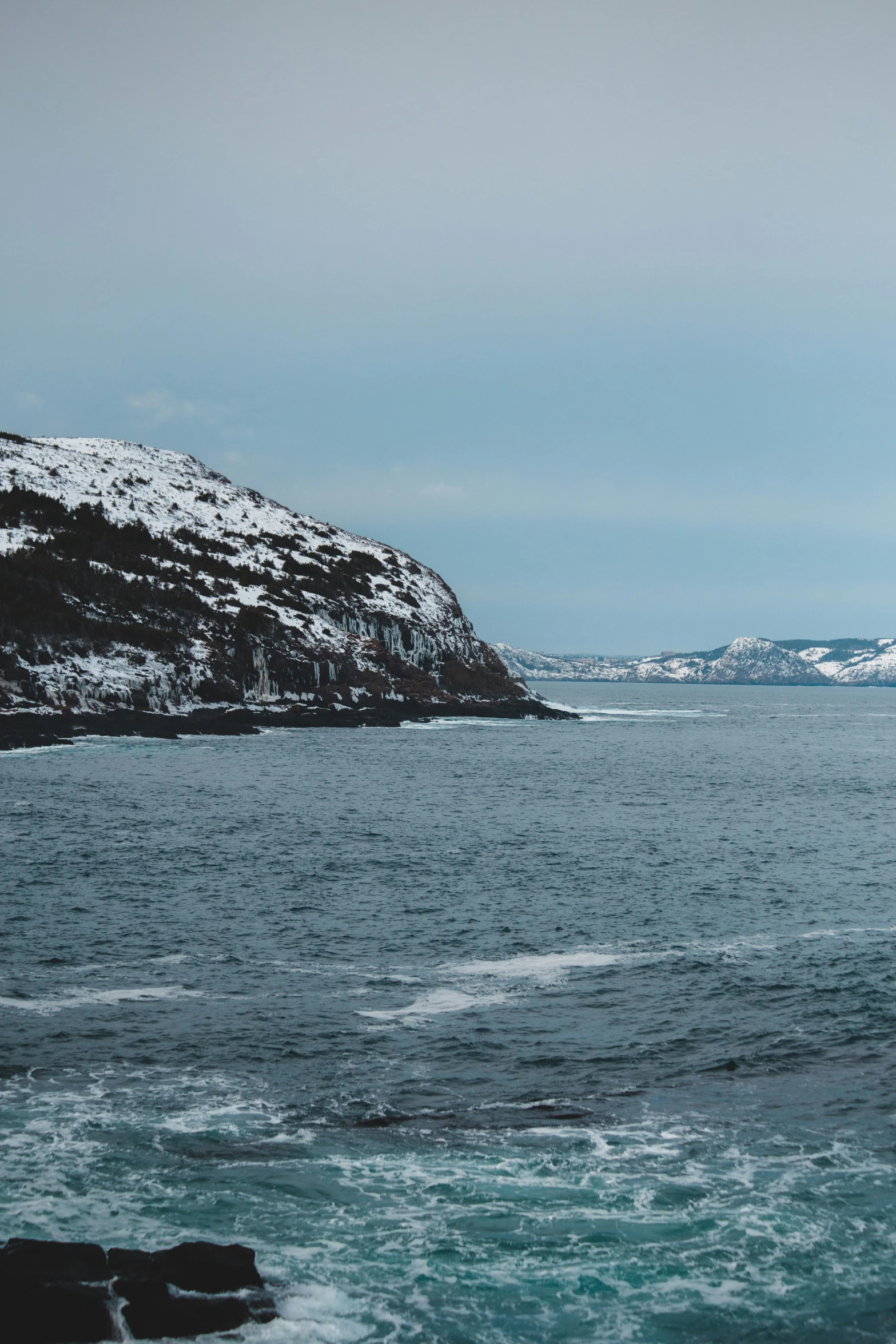 a body of water surrounded by snow covered mountains, by Roar Kjernstad, trending on unsplash, les nabis, coastal cliffs, low quality photo, quebec, harbour