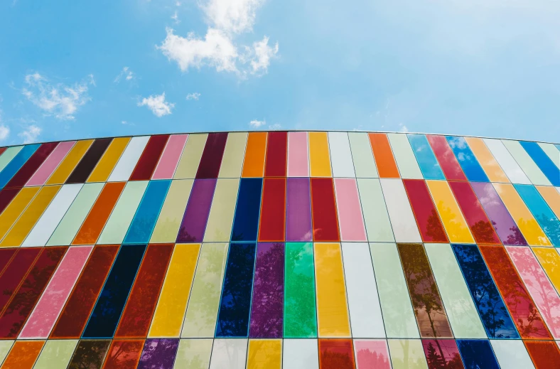 a colorful building with a blue sky in the background, a mosaic, inspired by Ellsworth Kelly, pexels contest winner, color field, lacquered glass, faded colours, colorful clouds