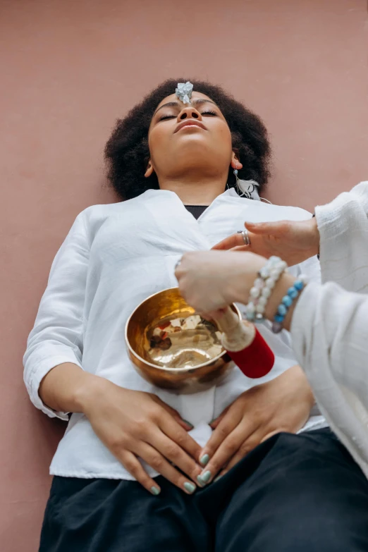 a woman in a white shirt is holding a bowl, trending on pexels, renaissance, opening third eye, lie on a golden stone, shambala, woman holding another woman