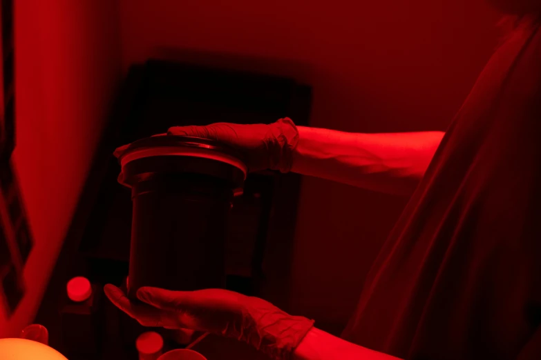 a person holding a cup in front of a red light, in laboratory, darkroom, sterile colours, coating a stubborn core.'