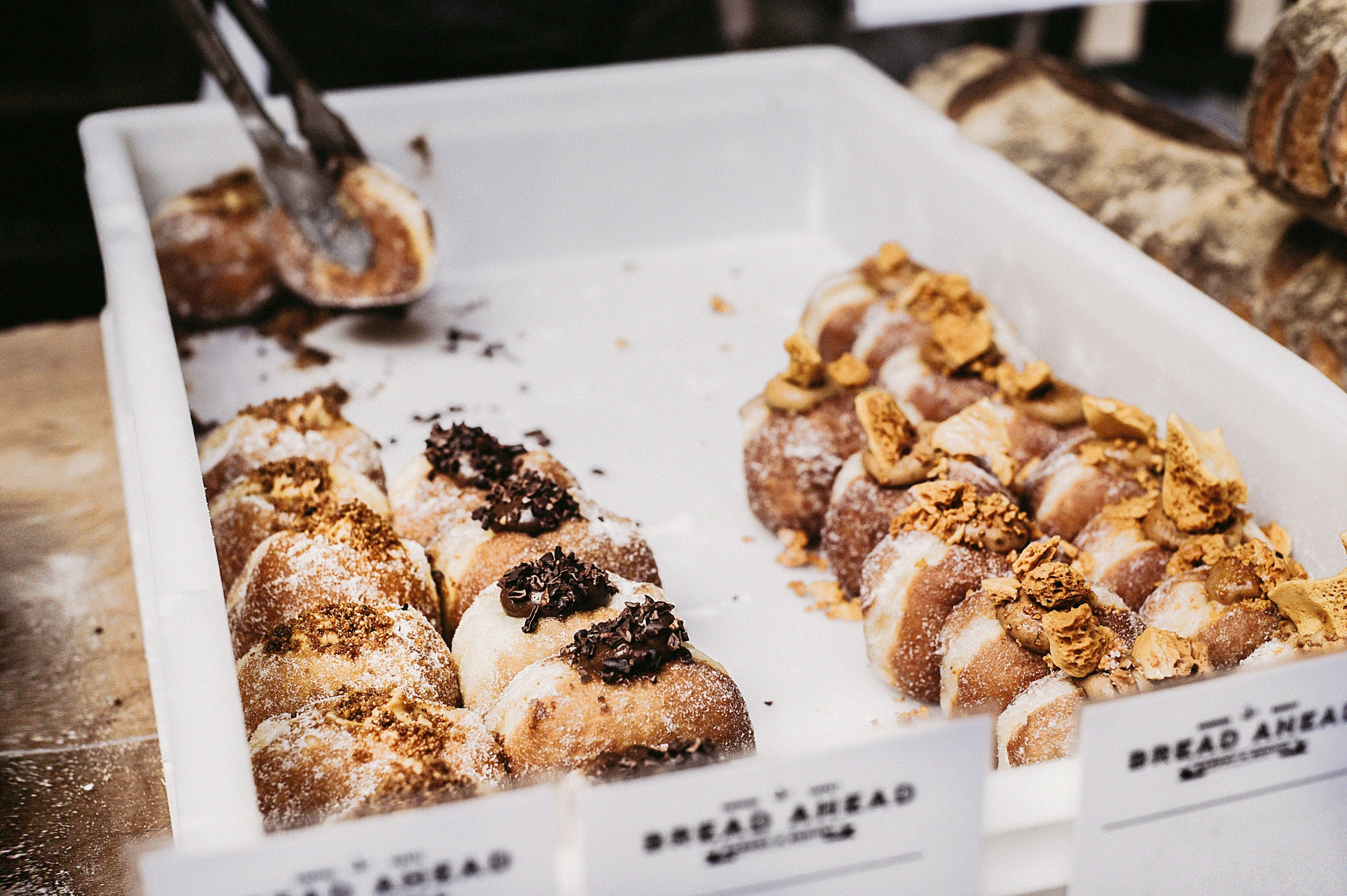 a box of doughnuts sitting on top of a table, food stall, browns and whites, sea of parfait, in a row